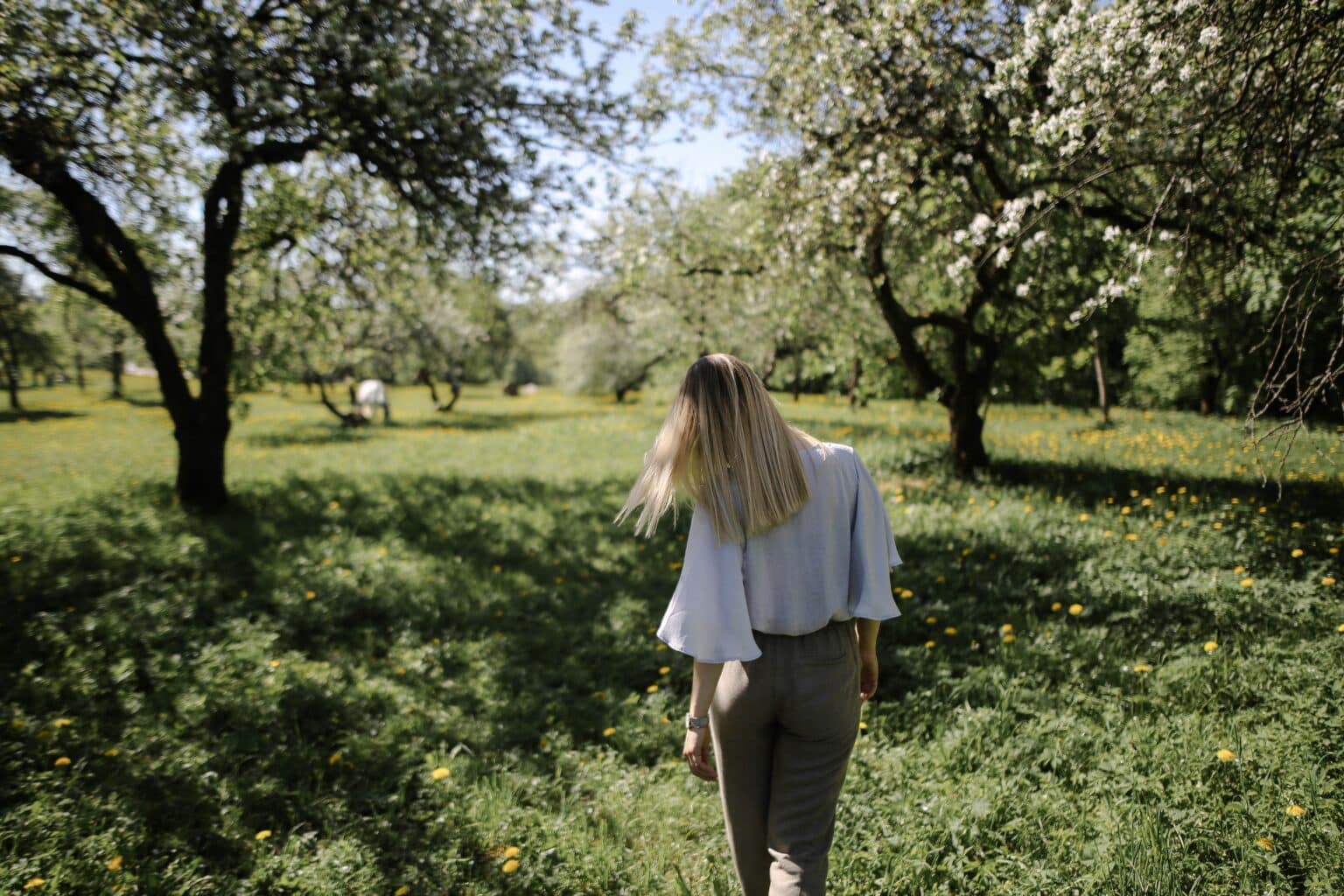 A young woman walking through a grassy park.